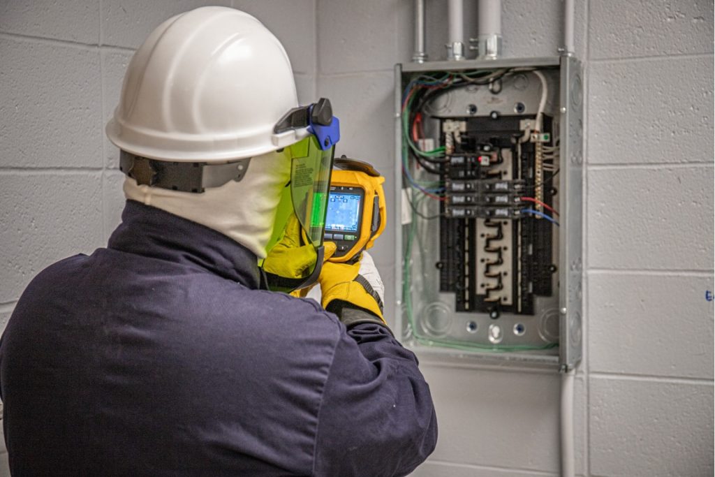 man in arc flash suit using infrared scanner